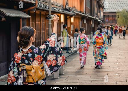 Japanisches Mädchen im Kimono, das ein Foto einer traditionellen Straße mit Holzhäusern auf ihrem Handy in Kanazawa Japan fotografiert Stockfoto