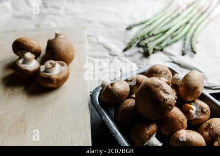 Hoher Winkel Haufen von braunen Pilzen auf Holztisch und grünen Spargelstängel auf Papier Stockfoto
