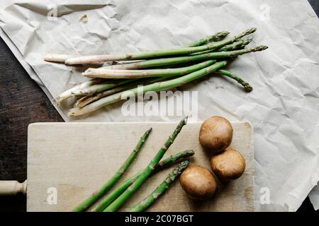 Von oben angeordnete rohe Stängel von Spargel auf Papier und frische Pilze auf dem Tisch zum Kochen Stockfoto