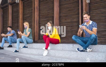 Junge Menschen mit Mobiltelefonen und halten soziale Distanz im Freien - multirassische Freunde Spaß haben, beobachten auf Smartphones sozialen Netzwerken Apps Stockfoto