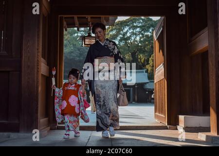 Mutter und kleine Tochter in traditionellen japanischen Kimonos, die durch ein Holztor am Meiji Jingu Schrein in Tokio gehen Stockfoto