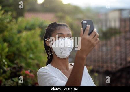 Junge schwarze Frau in Gesichtsmaske mit einem Smartphone Stockfoto