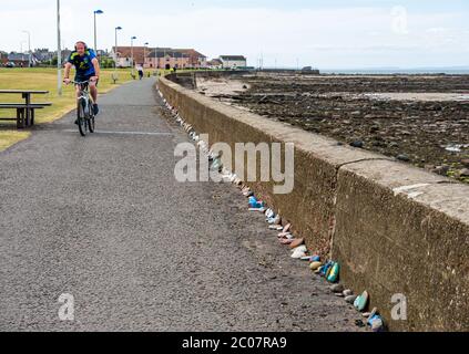 Port Seton, East Lothian, Schottland, Großbritannien. Juni 2020. Covid-19 Pandemiesymbole von Einheimischen: Eine hunderte Meter lange Linie an der Strandpromenade mit bunten und kreativen handbemalten Steinen mit inspirierenden Botschaften. Es scheint ein Phänomen zu sein, das sich in den Städten und Dörfern von East Lothian verbreitet. Ein Radfahrer radelt auf dem Fußweg an der Steinlinie vorbei Stockfoto