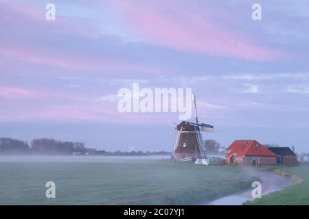 Alte Windmühle im Sonnenaufgangsnebel am Fluss Stockfoto