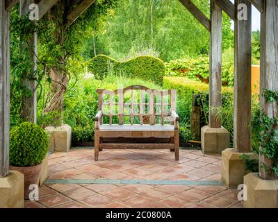 Leerer Holzgartensitz unter einer Pergola in Harlow Carr Gardens in Harrogate, Großbritannien Stockfoto