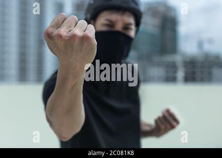 Ein Protestor, der mit einer Maske bedeckt war, wütend, mit seiner Faust in der Stadt stehend Stockfoto