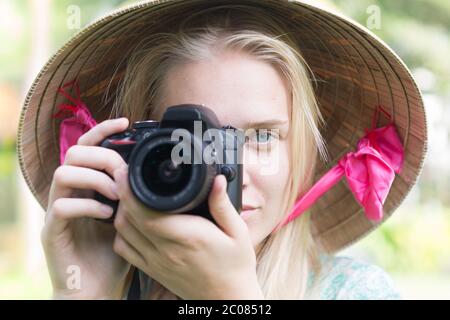 Eine schöne Frau mit blauen Augen aus der Nähe, hält eine Kamera und konzentriert sich auf ihre Aufnahme, die in das Objektiv schaut. Stockfoto
