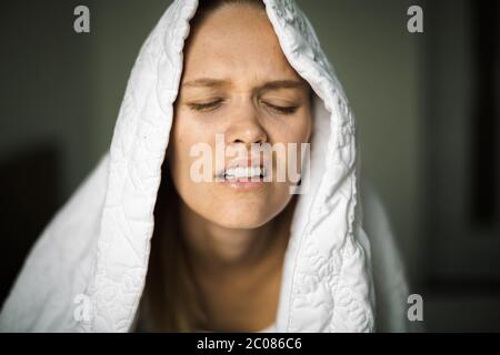 Eine müde, schläfrige Erwachsene im Bett, die Schlafprobleme in der Mitte der Nacht mit dem Kissen und der Decke über ihrem Kopf hatte. Schlafentzug. Stockfoto