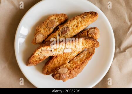 Italienische Cantucci-Kekse mit Mandeln auf einem weißen Teller mit einem Bastelpapier Hintergrund. Toskanische Biscotti. Traditionelle Cantuccini. Hausgemachte italienische Süßigkeiten Stockfoto