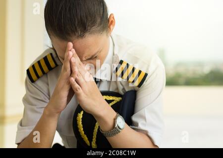 Eine Pilotin, die am Flughafen sitzt und einen schlechten Tag hat, besorgt und unter Angst leidet. Stockfoto