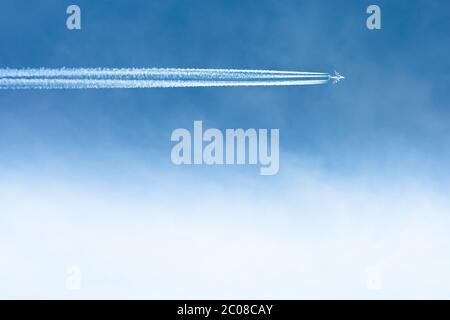 Ein kommerzielles Flugzeug, das über den klaren blauen Himmel mit Wolken und Kontrageln fliegt. Stockfoto