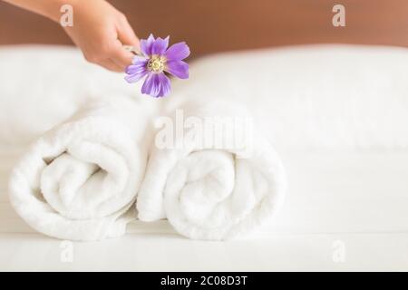 Ein Reinigungsservice, der eine lila Blume auf saubere weiße Laken und ein Set von zwei Rollhandtüchern in einem Hotelzimmer legt. Stockfoto