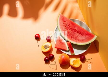 Trendige sommerliche Fruchtkomposition mit tropischen Blättern Schatten auf einem orange-gelben Set. Speicherplatz kopieren Stockfoto