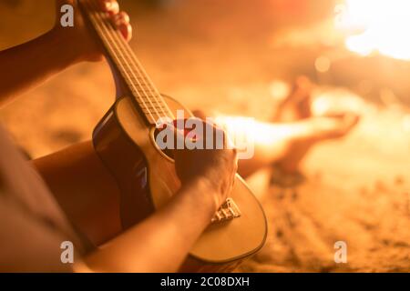 Eine Musikerin, die draußen Gitarre spielt, neben einem Feuer sitzt. Entspannung. Stockfoto