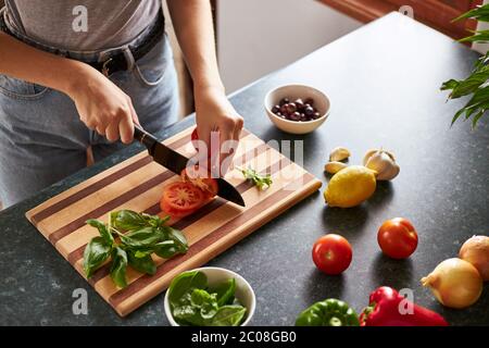 Nahaufnahme einer Frau, die eine Tomate auf einem Holzbrett zerhackt. Stockfoto