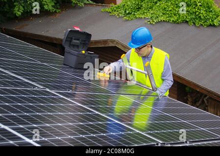 Installation und Inbetriebnahme von Solarmodulen. Erneuerbare Energie in einem privaten Zuhause. Arbeiter auf Leiter mit Elektrogeräten auf dem Dach. Ecologica Stockfoto