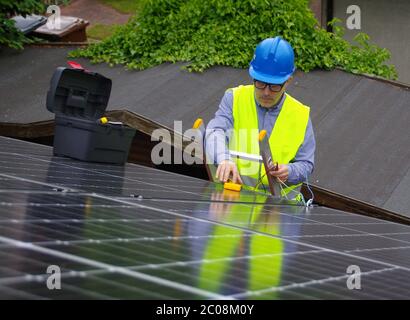 Installation und Inbetriebnahme von Solarmodulen. Erneuerbare Energie in einem privaten Zuhause. Arbeiter auf Leiter mit Elektrogeräten auf dem Dach. Ecologica Stockfoto