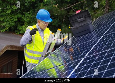 Installation und Inbetriebnahme von Solarmodulen. Erneuerbare Energie in einem privaten Zuhause. Arbeiter mit Elektrogeräten auf dem Dach. Stockfoto
