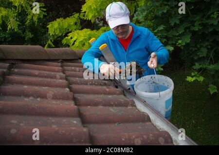 Mann auf der Leiter reinigt Rinne auf dem Dach. Wartung eines privaten Hauses. Stockfoto