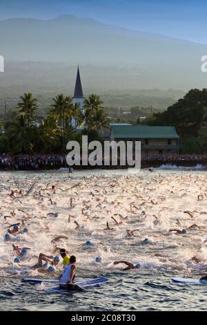 Schwimmen Start der Weltmeisterschaft Ironman Triathlon, Kailua Kona, Hawaii mit Mokuaikaua Kirche und Hualalai auf Hawaii Island. Stockfoto