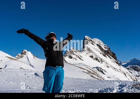 Mädchen genießen Wintersonnenstrahlen mit offenen Armen auf der Spitze der Bergkette. Snowboarder am späten Nachmittag in den Schweizer alpen im Winter. Nahaufnahme und Kontra Stockfoto