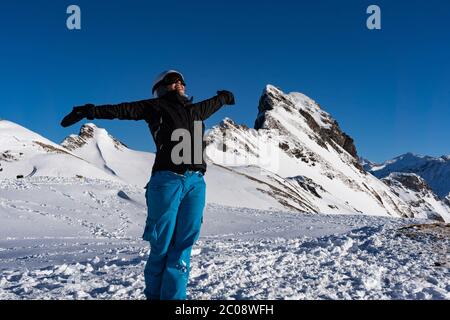 Mädchen genießen Wintersonnenstrahlen mit offenen Armen auf der Spitze der Bergkette. Snowboarder am späten Nachmittag in den Schweizer alpen im Winter. Konzept für expr Stockfoto