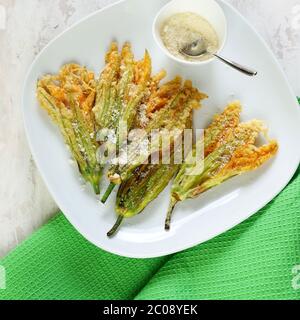 Gemüsekonzept. Zucchini Blumen gebraten in Teig und bestreut mit Parmesan Käse auf hellem Hintergrund. Draufsicht. Stockfoto