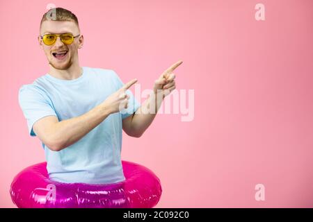 Glücklicher Mann in gelber Sonnenbrille zeigt Finger auf Copyspace und zwinkert Stockfoto