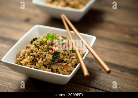 Basilikum gebratenen Reisschale mit Essstäbchen auf den Schalen auf Holzhintergrund gelegt ruhen. Dieses asiatisch inspirierte Rezept verwendet viele frische Zutaten. Stockfoto