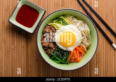 Blick von oben auf Bibimbap, ein klassisches koreanisches Essen. Reis wird mit gewürztem Gemüse, Fleisch und einem sonnigen Seite up Spiegelei auf der Oberseite gekrönt. Stockfoto