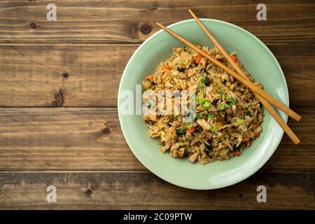 Basilikum-Hühnerreis mit Essstäbchen auf einem Holzhintergrund von oben betrachtet. Dieses thai-inspirierte Gericht ist perfekt für ein Mittagessen oder eine Beilage. Stockfoto