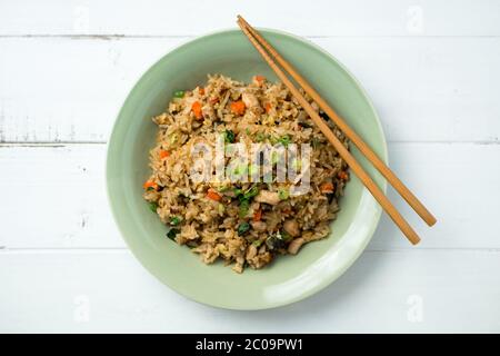 Basilikum-Hühnerreis mit Essstäbchen auf weißem Holzhintergrund von oben betrachtet. Dieses thai-inspirierte Gericht ist perfekt für ein schnelles Mittagessen oder Beilage. Stockfoto