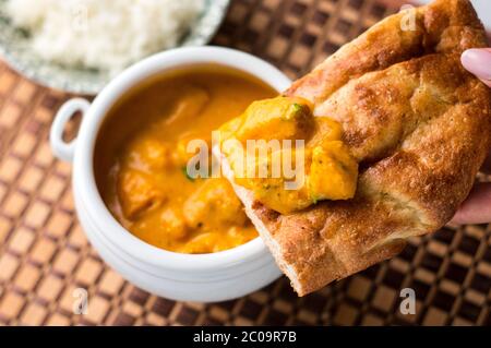 Nahaufnahme von einem leckeren indischen Butter-Hühnercurry auf einem Naan-Brot mit Reis auf einem hölzernen Tischset im Hintergrund. Stockfoto