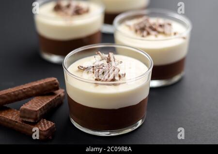 No-bake geschichtete Schokolade Mousse und Käsekuchen mit Schokolade überzogene Wafer Cookie Krümel Belag. In Dessertschüsseln aus klarem Glas. Auf dunklem Hintergrund. Stockfoto