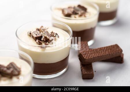 No-bake geschichtete Schokolade Mousse und Käsekuchen mit Schokolade überzogene Wafer Cookie Krümel Belag. In Dessertschüsseln aus klarem Glas. Auf weißem Hintergrund. Stockfoto