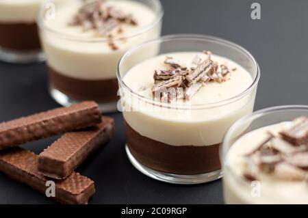 No-bake geschichtete Schokolade Mousse und Käsekuchen mit Schokolade überzogene Wafer Cookie Krümel Belag. In Dessertschüsseln aus klarem Glas. Auf dunklem Hintergrund. Stockfoto