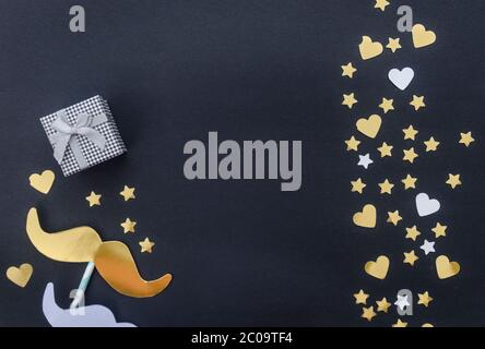 Happy Father's Day Konzept - Schnurrbart, Gegenwart und goldene Sterne auf schwarzem Hintergrund. Flach liegend, Draufsicht, Kopierbereich. Stockfoto