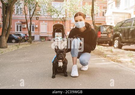 Frau in medizinischen Maske und Latexhandschuhe berühren niedlichen französisch Bulldogge auf der Straße Stockfoto