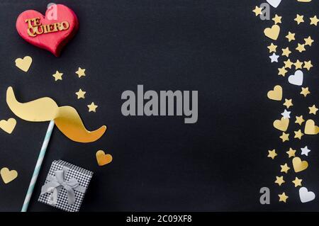 Vatertag Konzept - Geschenk, Schnurrbart, Herz und Sterne auf schwarzem Hintergrund mit dem Wort auf spanisch für "Ich liebe dich". Flach liegend, Draufsicht, Kopierbereich. Stockfoto