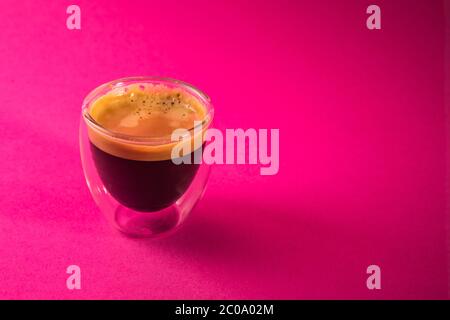 Frisch gebrühter cremiger Espresso in einer Tasse aus Glas, isoliert auf rosa Hintergrund, Nahaufnahme mit Kopierraum Stockfoto