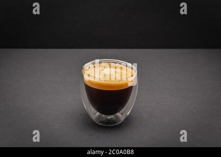 Frisch gebrühter cremiger Espresso in einer Tasse mit Glas, isoliert auf grauem und schwarzem Hintergrund, Nahaufnahme mit Kopierraum Stockfoto