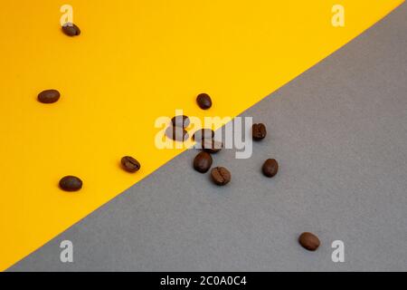 Verschüttete geröstete braune Kaffeebohnen isoliert auf gelbem und grauem Hintergrund, Nahaufnahme mit Kopierraum Stockfoto