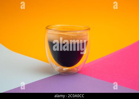Frisch gebrühter cremiger Espresso in einer Kaffeetasse aus Glas, isoliert auf farbigem Hintergrund, Nahaufnahme mit Kopierraum Stockfoto