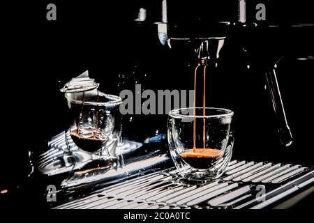 Dunkler Kaffee aus einer manuellen Espressomaschine in eine Espressotasse aus transparentem Glas gießen, mit Platz für Kopien, Nahaufnahme Stockfoto