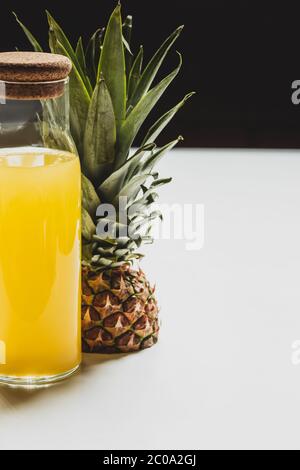 Frischer Ananassaft in der Flasche in der Nähe von Schnitt köstliche Frucht auf weißer Oberfläche auf schwarz isoliert Stockfoto