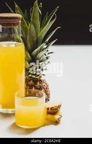 Frischer Ananassaft in Flasche und Glas in der Nähe geschnitten köstliche Frucht auf weißer Oberfläche auf schwarz isoliert Stockfoto