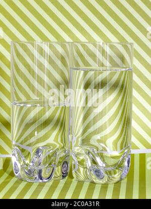 Glas Wasser vor gestreiftem Hintergrund, Wasser im brechenden Licht Stockfoto