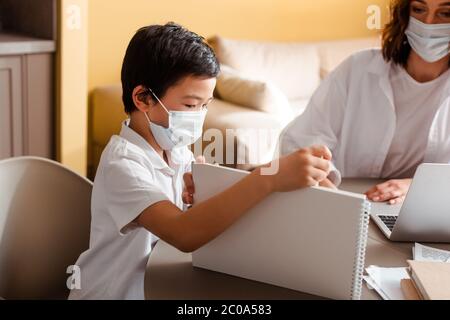 asiatische junge in medizinischen Maske Studium mit Mutter zu Hause auf Quarantäne Stockfoto