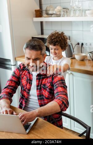 Selektiver Fokus von schönen freiberuflichen Vater mit Laptop in der Nähe lockigen Sohn Stockfoto