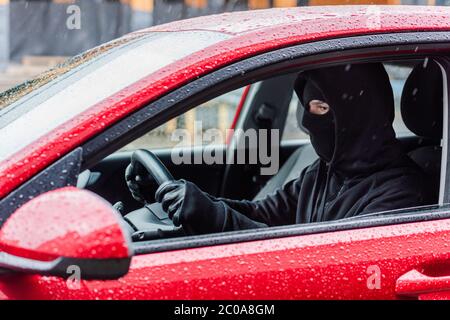 Seitenansicht des Räubers in Lederhandschuhen und Sturmhaube, die im Auto bei Regen sitzt Stockfoto